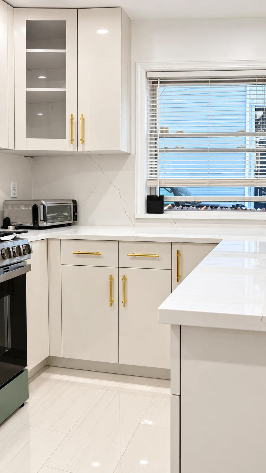 White kitchen cabinetry with polished gold handles and light stone countertop